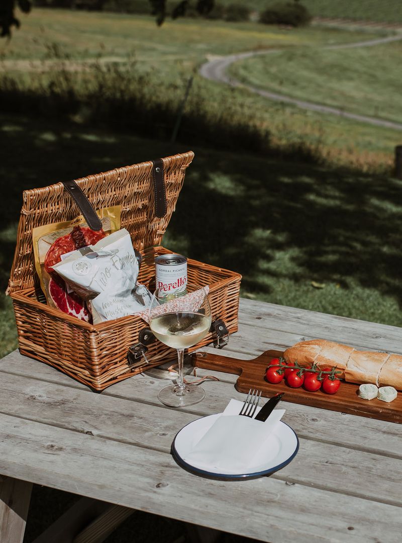 Picnic basket with food and wine on a wooden table outdoors