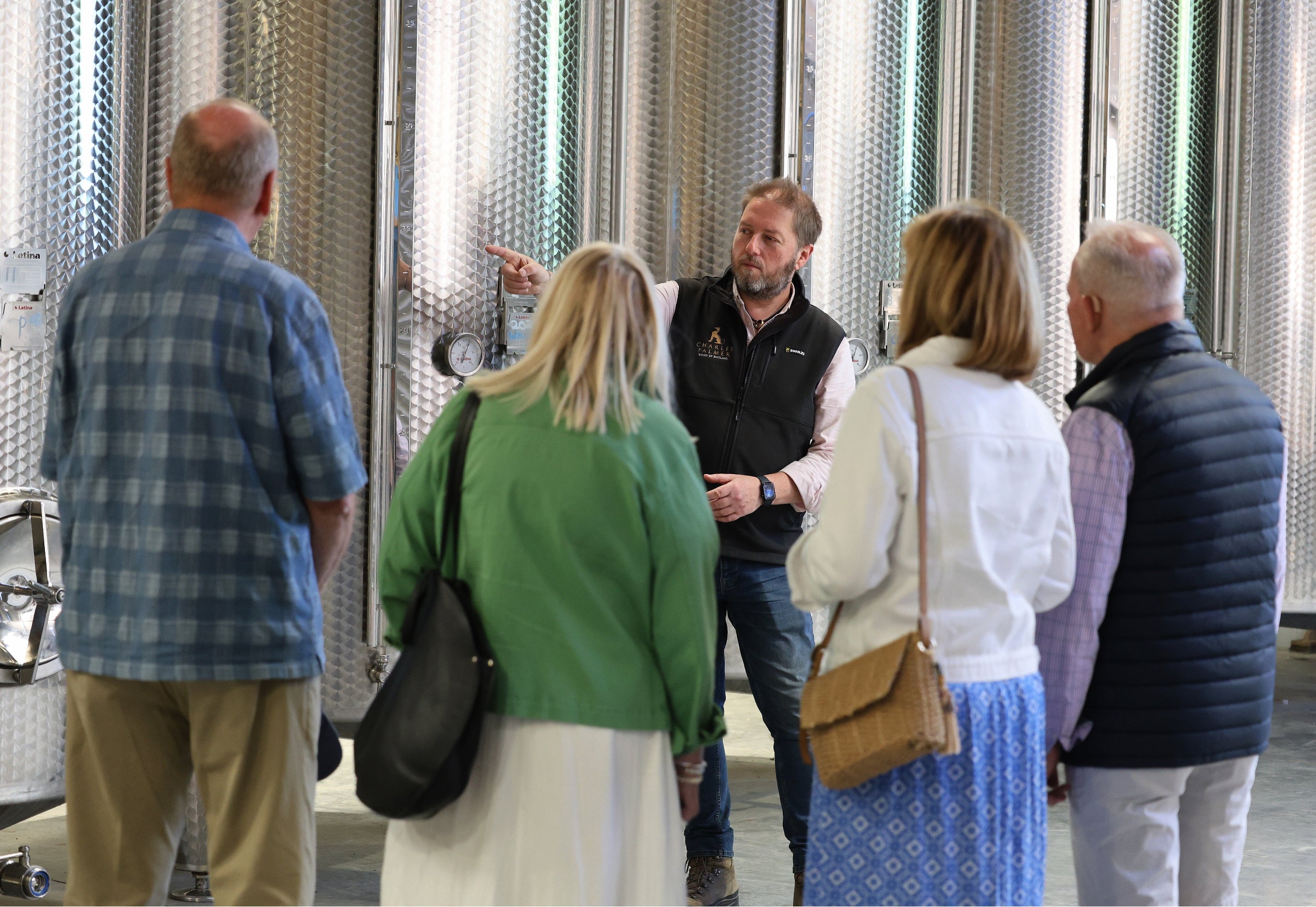 Group of people listening to a guide in front of large metal tanks.