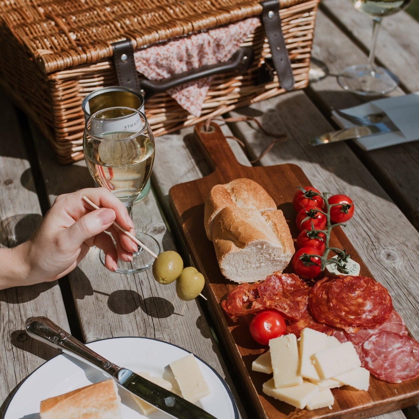 Picnic setup with wicker basket, charcuterie board, and wine on a wooden table.