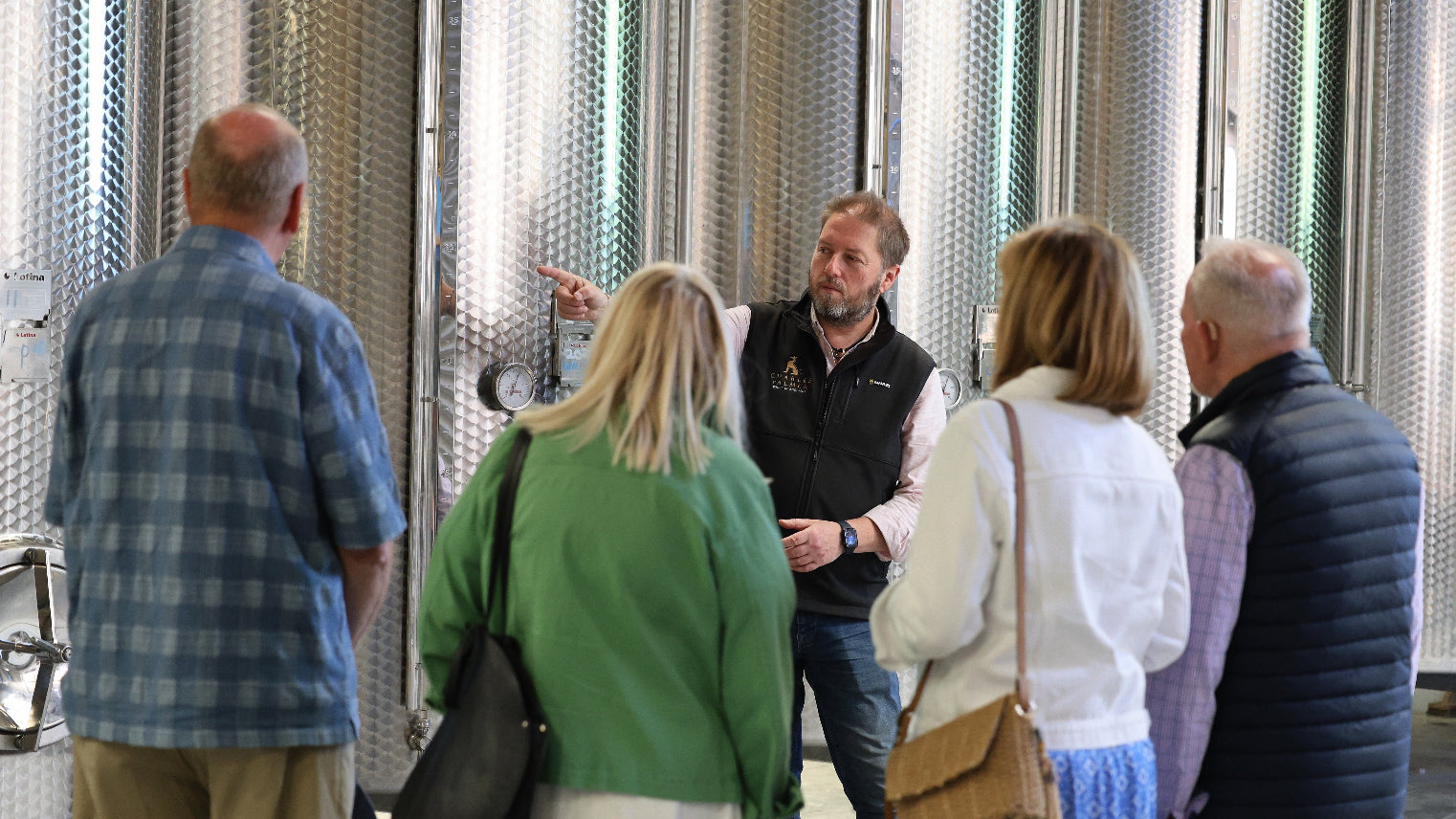 Group winery tour in front of large metal fermenting tanks